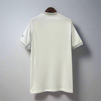 White t-shirt hanging on a black metal frame against a geometric patterned wall.